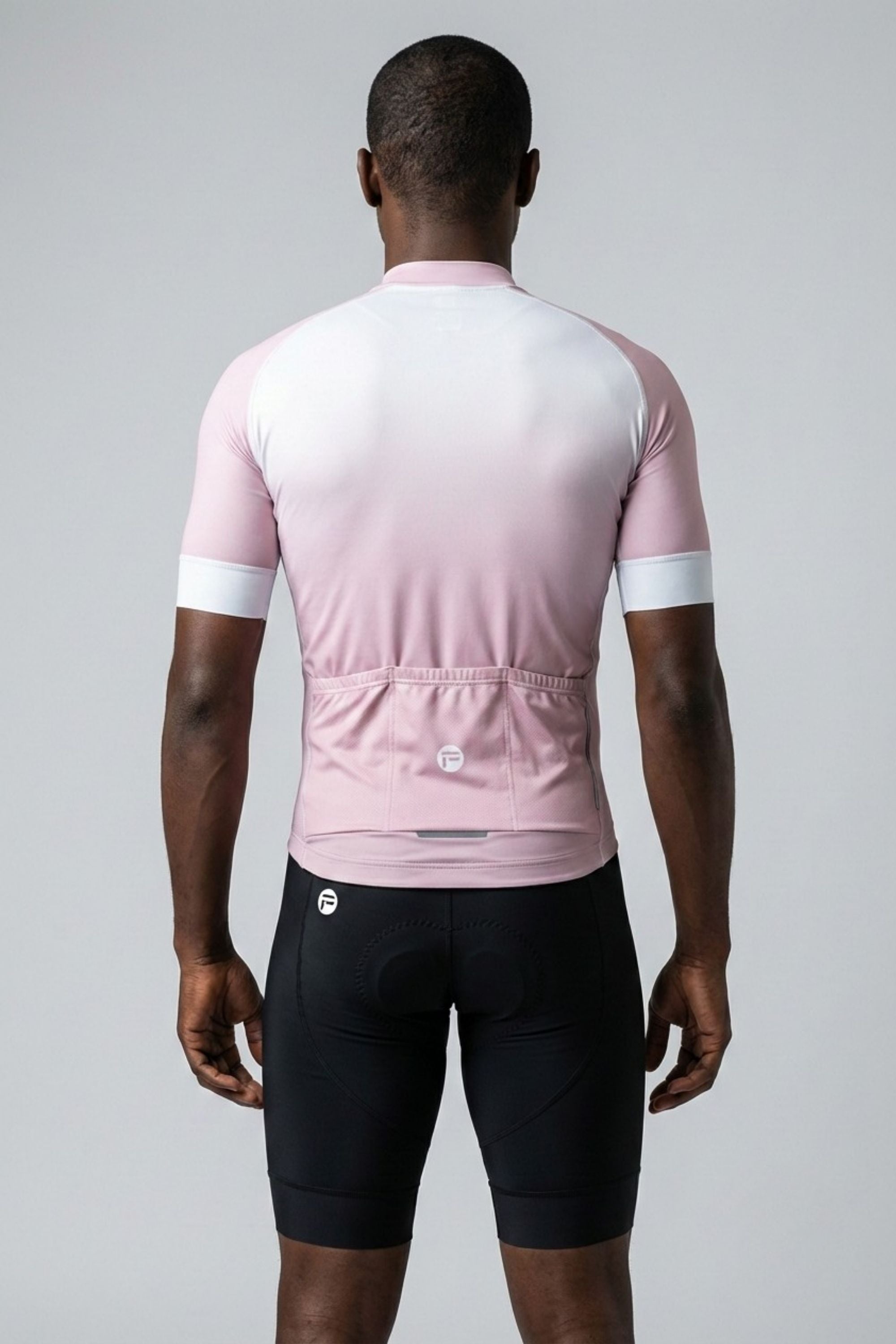 Person wearing a pink and white cycling jersey with black shorts on a gray background