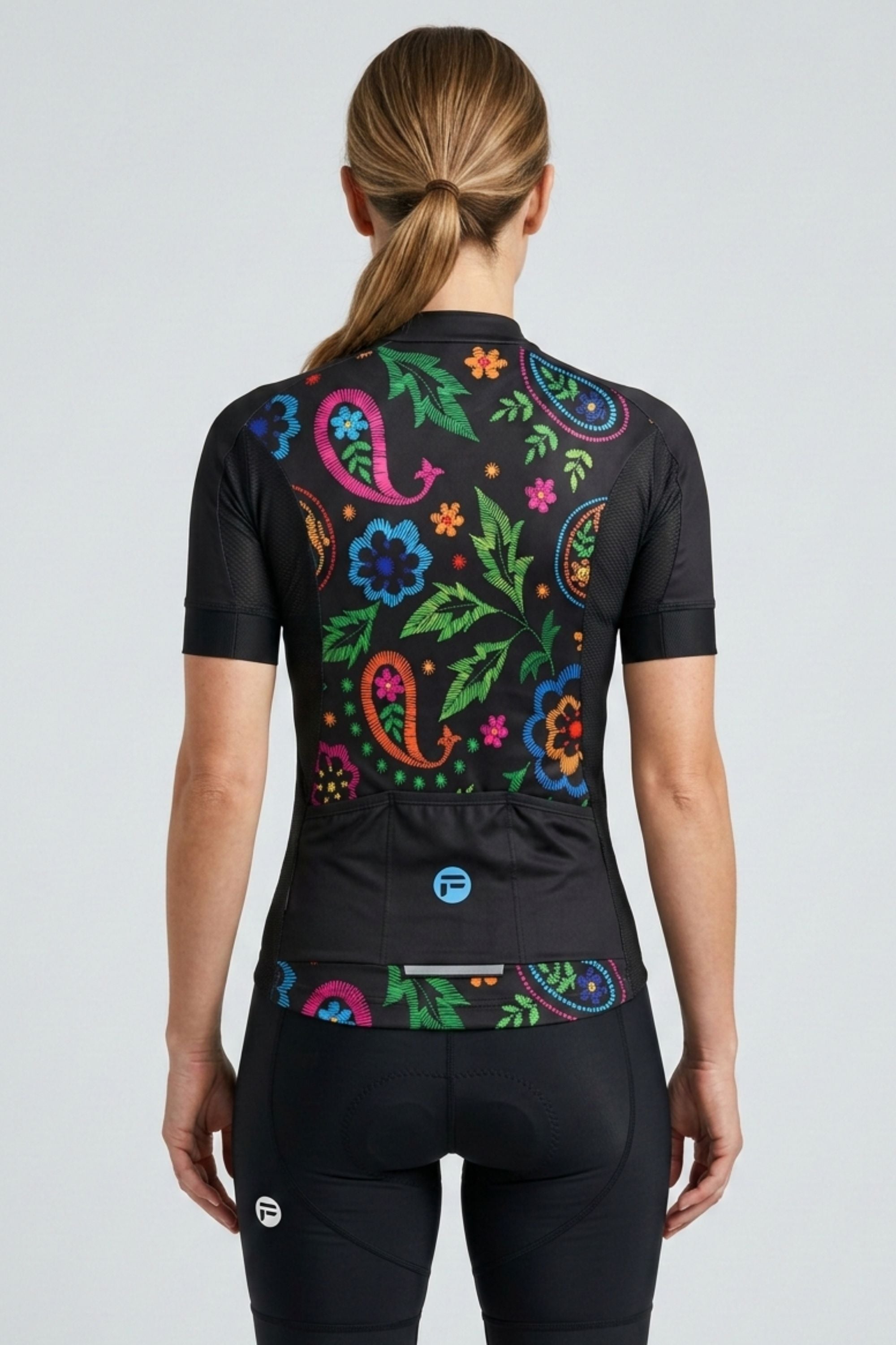 Person wearing a black cycling outfit with colorful floral patterns on the back against a light gray background