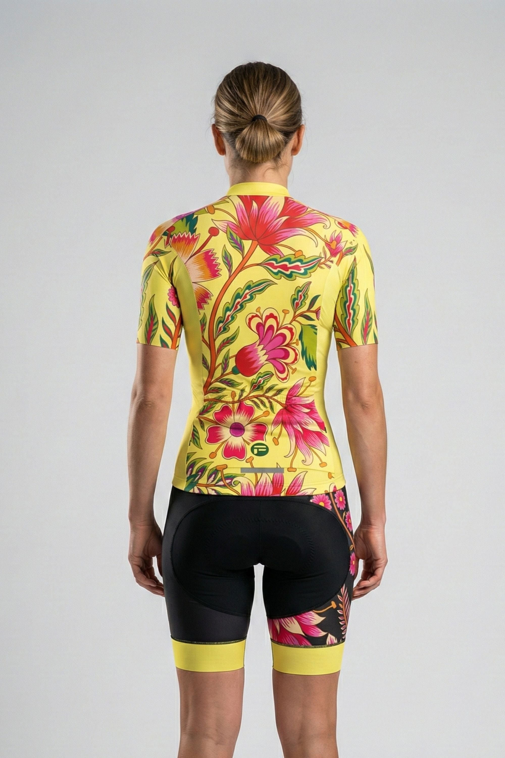Person wearing a yellow cycling outfit with pink flowers on a plain background by Cycling Frelsi