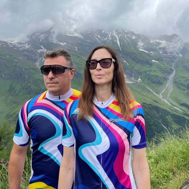 A man and a woman wearing Rainbow Sprinter cycling jerseys in front of the Austrian Alps