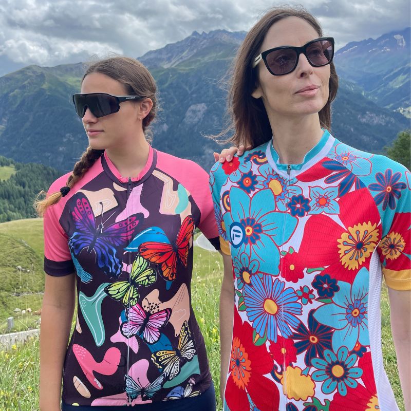 Cycling Frelsi's "Riding with Butterflies" and "Colorful Flowers" collection comes alive in this striking image of two female cyclists. The jerseys' intricate floral and butterfly designs add a touch of whimsy to their trek through the rugged mountain terrain.