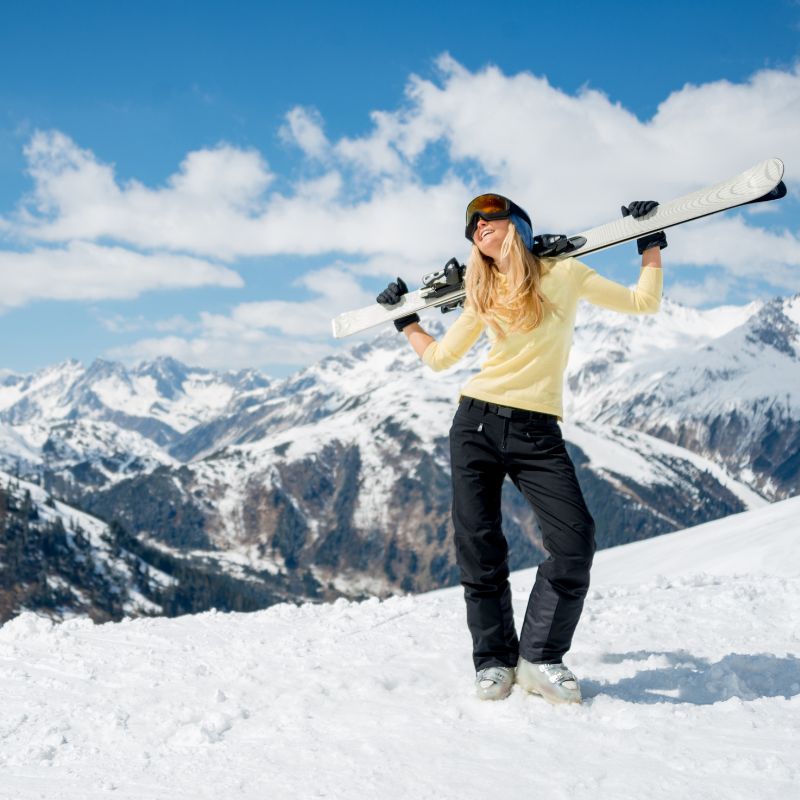 Hitting the slopes in style: A confident snowboarder, her yellow Cycling Frelsi shirt a beacon against the snowy expanse, poses atop a mountain, snowboard ready for the exhilarating descent. (Image of Woman posing on top of mountain with snowboard in yellow shirt)