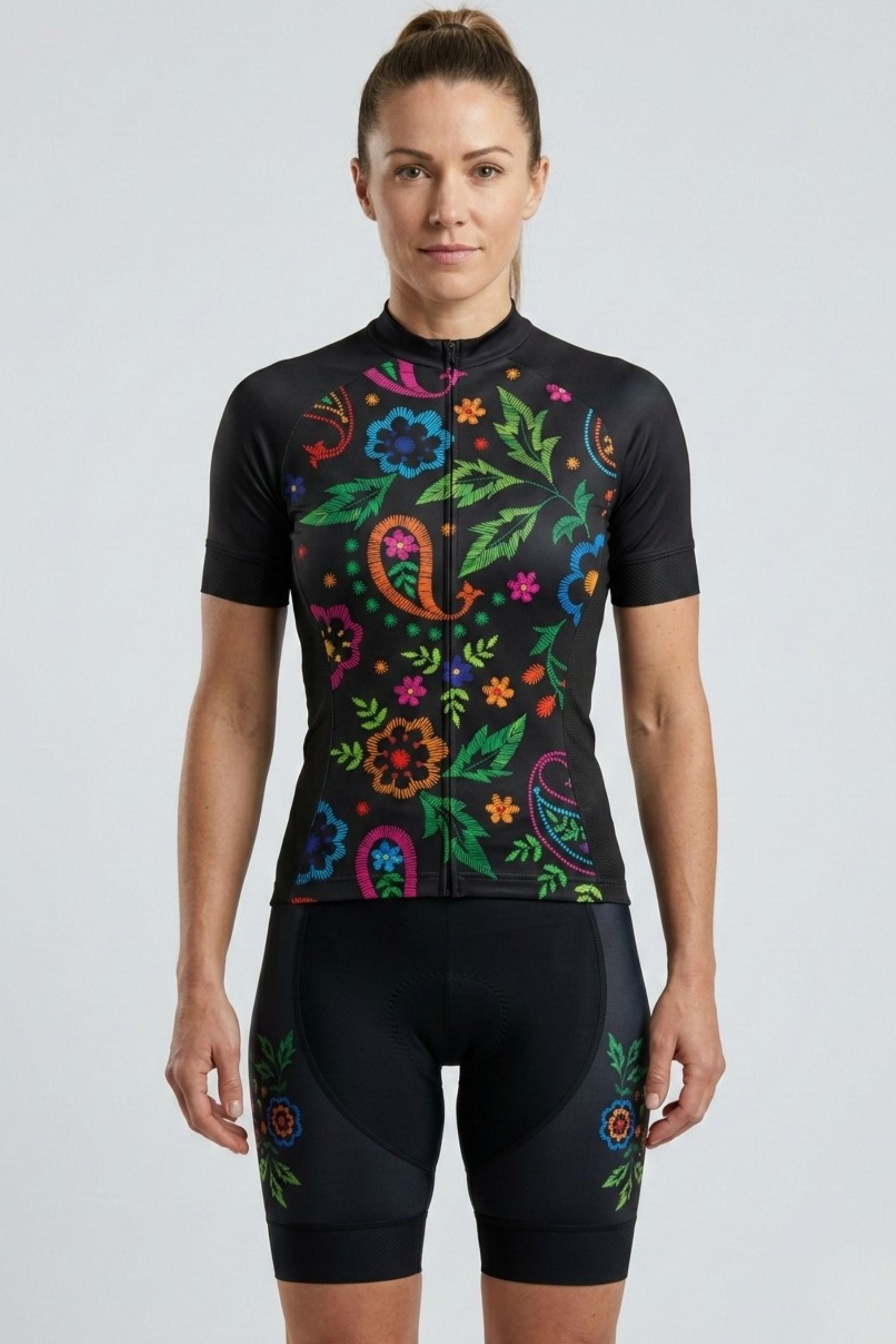 Woman wearing a black cycling outfit with colorful floral patterns on a light gray background