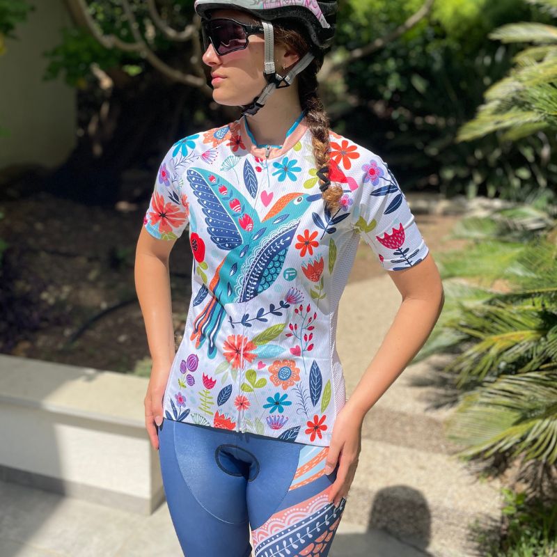 Woman wearing a vibrant short sleeve cycling jersey with a colorful bird and floral design, paired with matching blue cycling shorts. Ideal for warm-weather rides, blending style and comfort