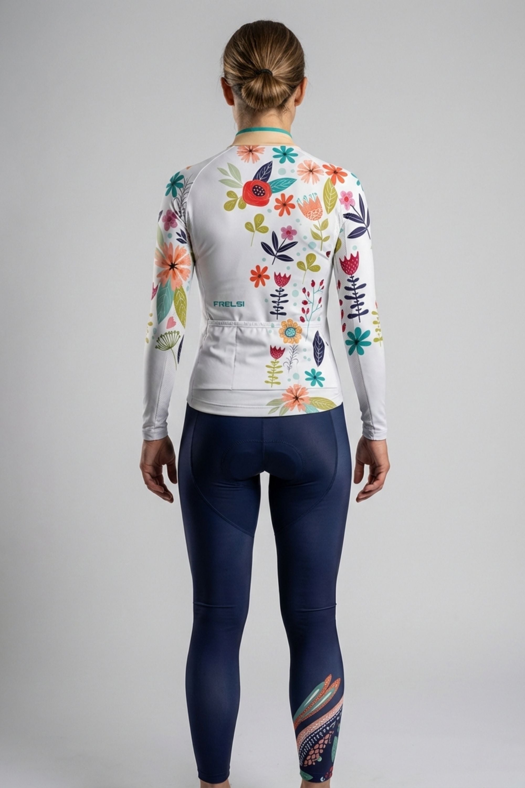 Person wearing a white cycling set with a blue bird and flowers accents by Cycling Frelsi on a gray background