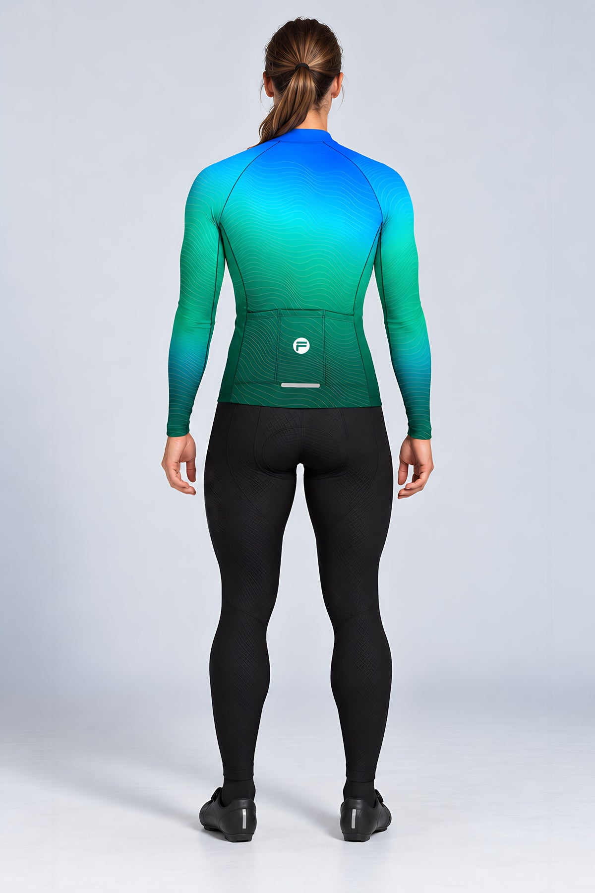 Woman wearing the Ocean Pulse long sleeve cycling jersey with black bib tights - back view