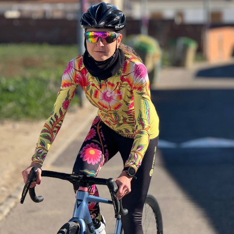 Woman cyclist wearing the vibrant Wildflower Ride cycling kit from Cycling Frelsi, riding a road bike on a sunny day.