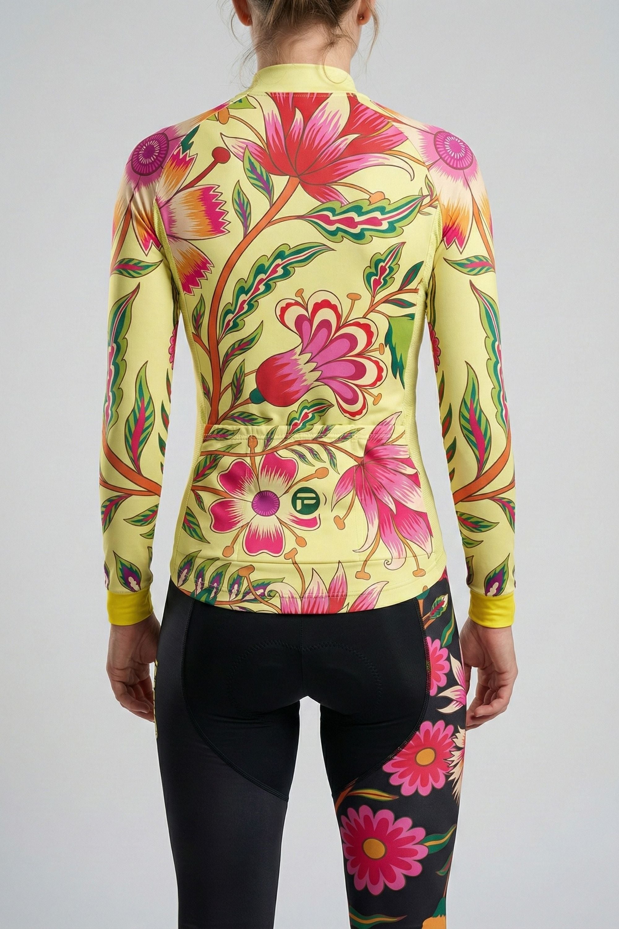 Person wearing a yellow cycling set with pink flowers colorful butterfly accents by Cycling Frelsi on a gray background