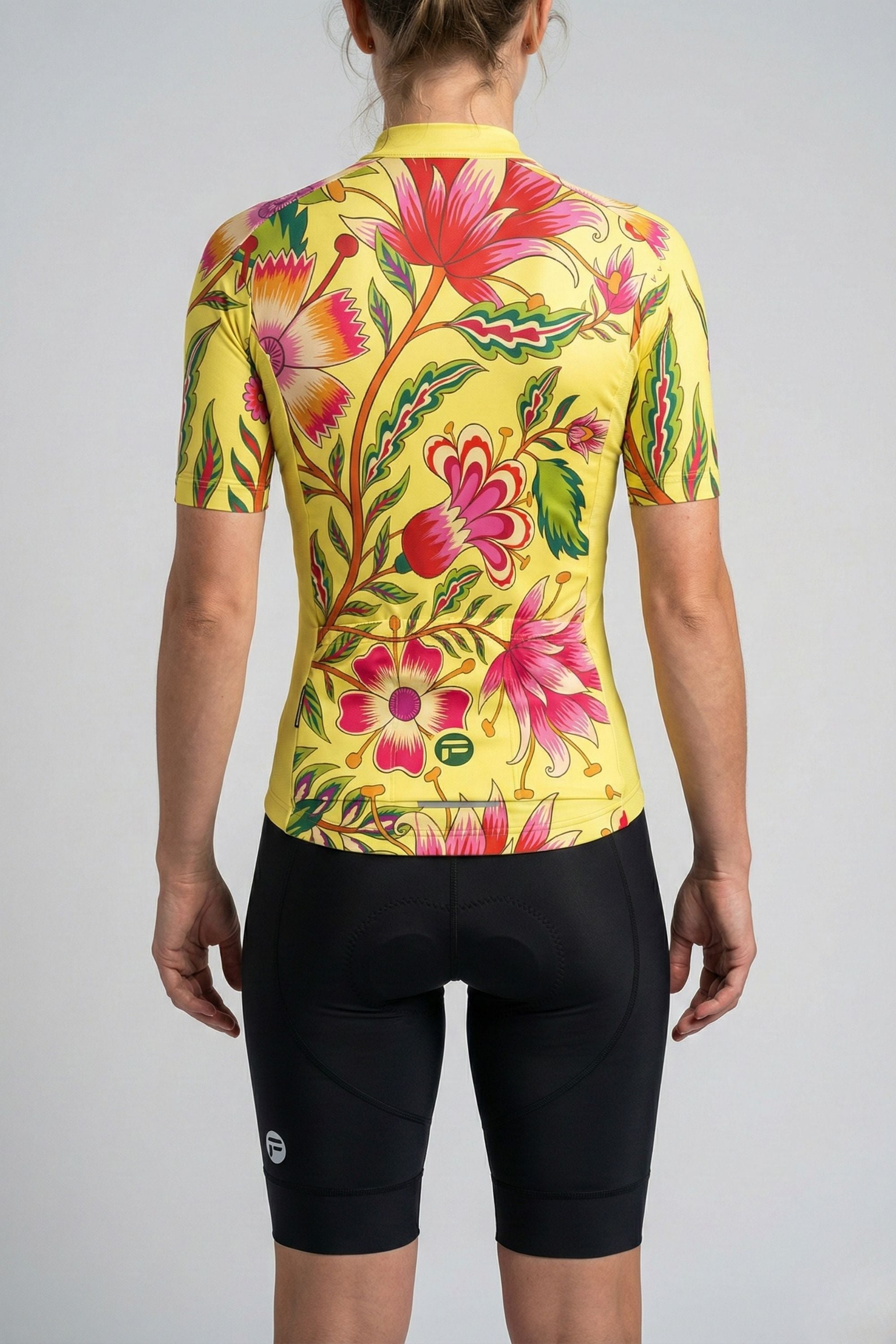 Person wearing a yellow cycling jersey with pink flowers accents by Cycling Frelsi on a gray background